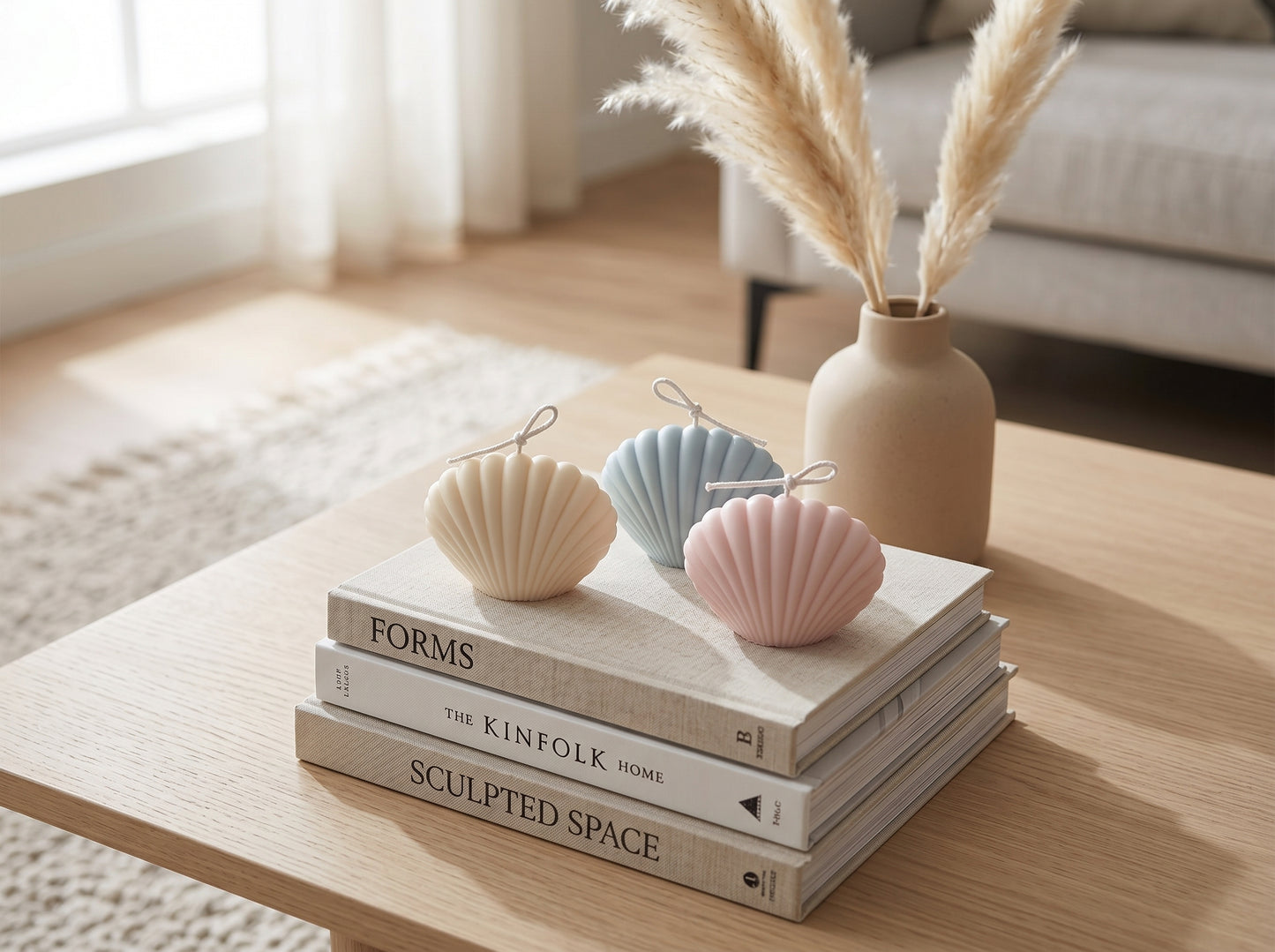 Decorative shell-shaped candles on books with a vase containing dried plants on a wooden table.